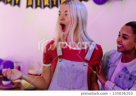 Surprised young woman celebrating birthday with friend at festive party Surprised young woman celebrating birthday with friend at festive party 135636103