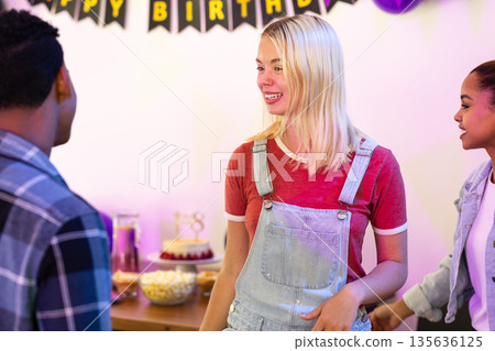 Friends celebrating birthday party, laughing and chatting near decorated table 135636125