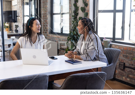 Colleagues discussing project ideas at office table with laptop and notebook 135636147