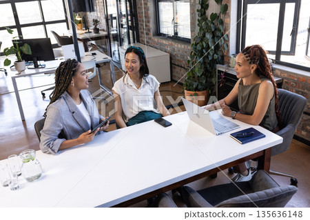 Colleagues discussing project ideas at office table with laptops and tablets 135636148