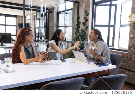 Businesswomen celebrating success with high-five in modern office meeting room Businesswomen celebrating success with high-five in modern office meeting room 135636150