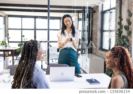 Smiling businesswoman leading meeting with colleagues in modern office setting 135636154