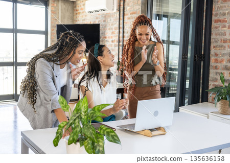 Colleagues celebrating success at office, smiling and clapping near laptop 135636158