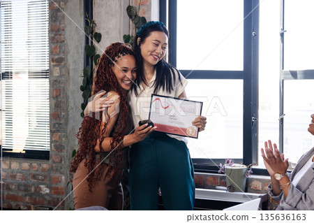 Asian woman holding certificate hugging colleague in office, celebrating achievement Asian woman holding certificate hugging colleague in office, celebrating achievement 135636163