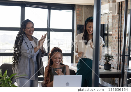 Celebrating success, diverse women cheering and clapping around laptop in office Celebrating success, diverse women cheering and clapping around laptop in office 135636164
