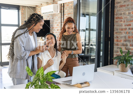 In office, diverse businesswomen cheering around laptop, celebrating success together In office, diverse businesswomen cheering around laptop, celebrating success together 135636178