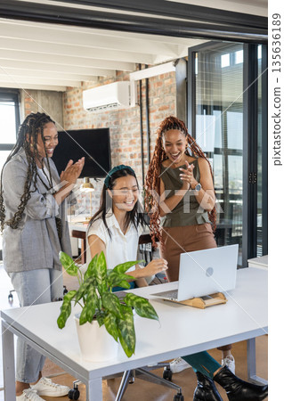 Team celebrating success at office, three women clapping and smiling at laptop Team celebrating success at office, three women clapping and smiling at laptop 135636189