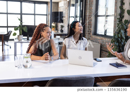 African American and Asian women in office meeting, smiling and discussing ideas 135636190