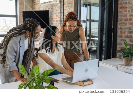 Collaborating on laptop, diverse businesswomen discussing project ideas in modern office 135636204