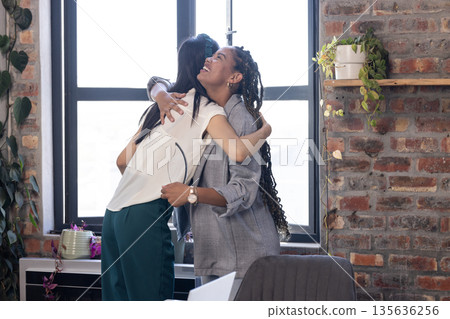 African American woman and colleague hugging in office, celebrating success together African American woman and colleague hugging in office, celebrating success together 135636256