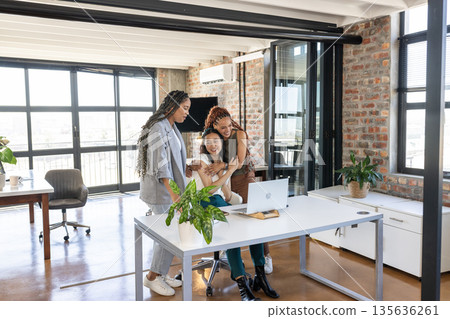 Colleagues celebrating success at office, smiling and embracing near laptop 135636261