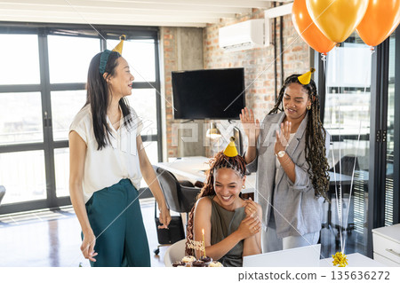 Celebrating birthday at office, colleagues wearing party hats and sharing cupcakes 135636272