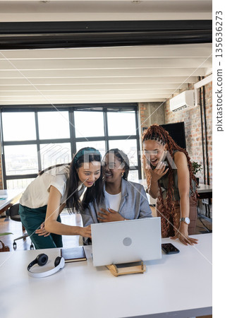 Diverse team celebrating success while looking at laptop in modern office 135636273