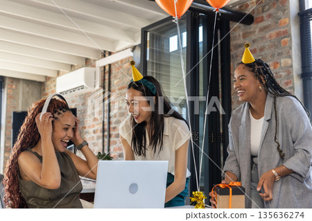 Colleagues celebrating success at office party with laptop and festive hats Colleagues celebrating success at office party with laptop and festive hats 135636274