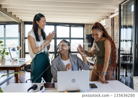Colleagues celebrating success at office, smiling and clapping around laptop Colleagues celebrating success at office, smiling and clapping around laptop 135636280