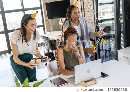 Celebrating birthday in office, colleagues wearing festive hats and sharing cupcakes 135636286