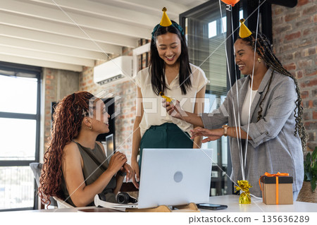 Colleagues wearing party hats celebrating with gifts and laughter in modern office 135636289