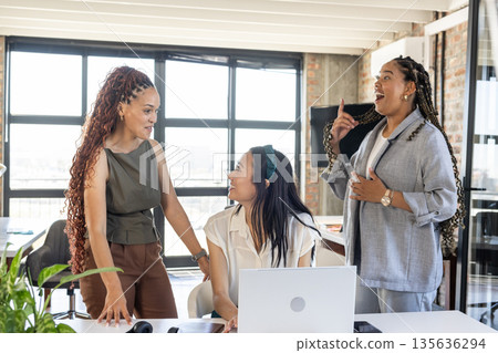 Celebrating success in office, colleagues smiling and discussing project around laptop Celebrating success in office, colleagues smiling and discussing project around laptop 135636294