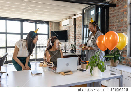 Celebrating birthday in office, colleagues wearing party hats with cupcakes, balloons Celebrating birthday in office, colleagues wearing party hats with cupcakes, balloons 135636306
