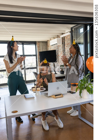 Celebrating birthday in office, colleagues wearing party hats and enjoying cupcakes 135636308