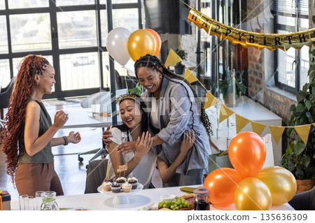 Colleagues celebrating birthday in office with cupcakes and festive decorations 135636309