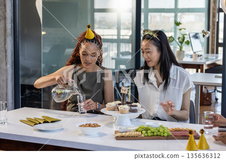 At office, diverse women celebrating with snacks and drinks during business party 135636312