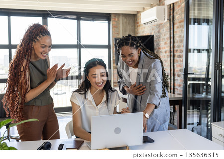Colleagues celebrating success at office, smiling and clapping around laptop 135636315