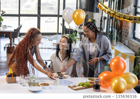 Colleagues celebrating birthday with cupcakes and balloons in modern office setting 135636316