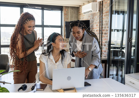 Colleagues celebrating success around laptop in modern office, sharing joyful moment Colleagues celebrating success around laptop in modern office, sharing joyful moment 135636317