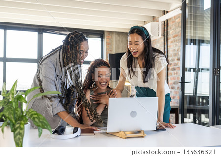 Colleagues celebrating success while looking at laptop in modern office 135636321
