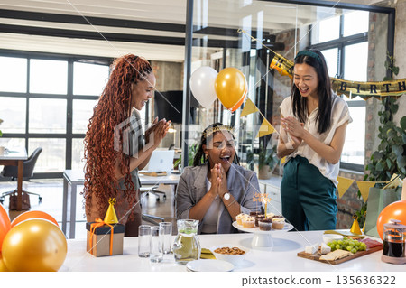 Colleagues celebrating birthday with cake and balloons in modern office setting 135636322