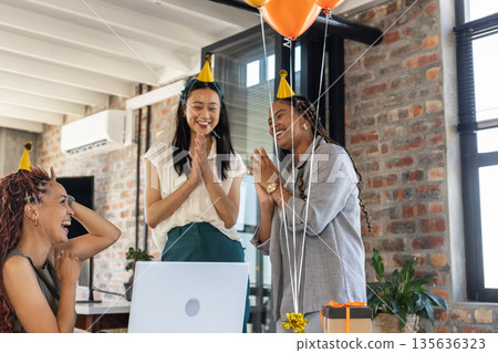Colleagues celebrating success with party hats and balloons in modern office 135636323