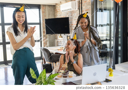 Celebrating birthday at office, colleagues wearing party hats and smiling with cupcakes 135636328