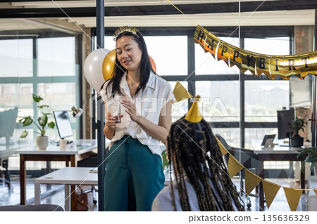 Businesswoman giving speech at office birthday party, holding glass and smiling 135636329