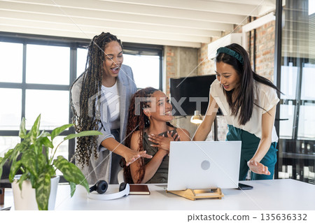 Celebrating success, colleagues expressing joy and excitement around laptop in office 135636332