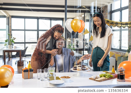 Colleagues celebrating birthday in office with balloons, cake, and joyful smiles 135636334
