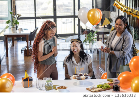 Colleagues celebrating birthday with cupcakes and balloons in modern office setting 135636338