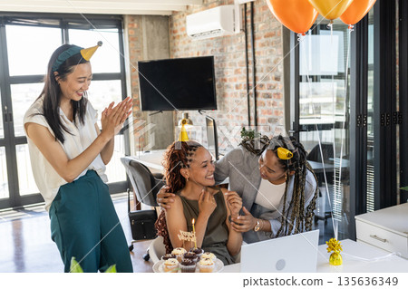 Celebrating birthday in office, colleagues wearing party hats and sharing cupcakes 135636349