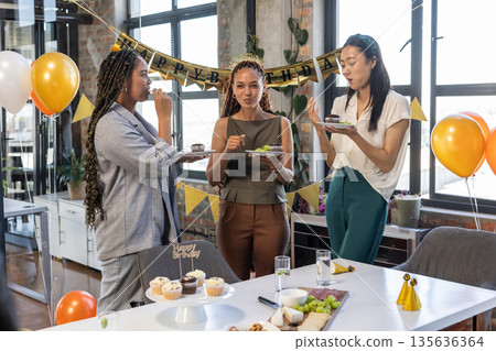 Colleagues enjoying birthday celebration with cake and balloons in modern office 135636364