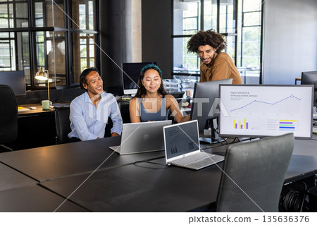 Team collaborating in modern office, analyzing graphs on laptops and monitor Team collaborating in modern office, analyzing graphs on laptops and monitor 135636376