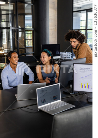 Diverse team collaborating on project with laptops and charts in modern office 135636377