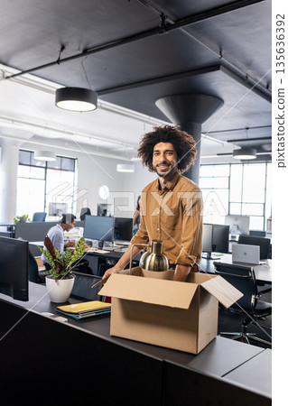 Smiling man unpacking box at modern office desk, starting new job 135636392