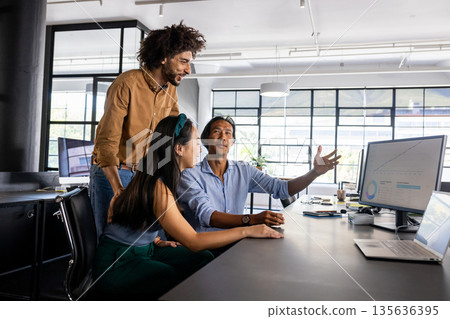 Diverse business team discussing project at office desk, analyzing data on computer Diverse business team discussing project at office desk, analyzing data on computer 135636395