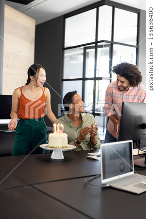 Celebrating birthday at office, diverse colleagues smiling around cake with candles 135636400