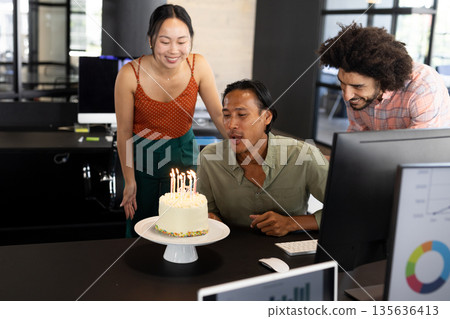 Colleagues celebrating birthday in office, man blowing out candles on cake 135636413