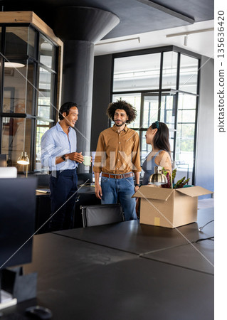 Colleagues in modern office chatting and smiling near unpacked box on desk 135636420