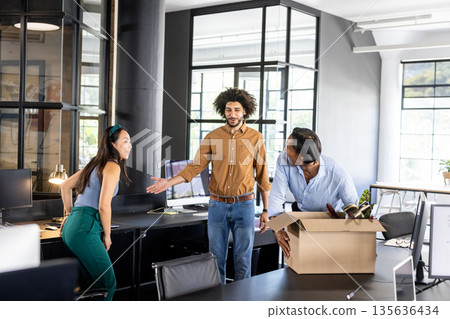 Colleagues welcoming new team member with box of belongings in modern office 135636434