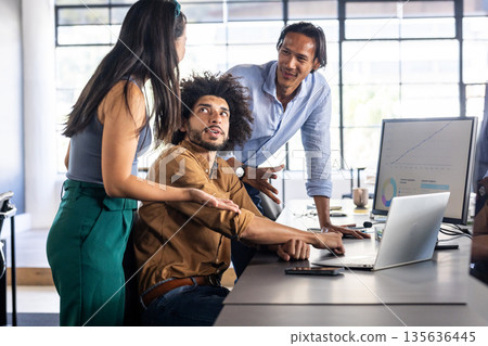 Collaborating in office, diverse team discussing project with laptop and charts 135636445
