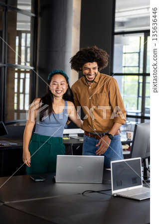 Colleagues in modern office smiling and collaborating on laptop project 135636446