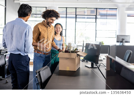 Colleagues unpacking welcome gift box in modern office, smiling and chatting 135636450